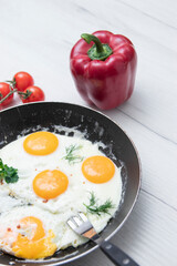 Scrambled eggs in frying pan bell pepper, cherry tomato on the background of a light wooden table. National Ukrainian or belorussian food. Breakfast, lunch. Top view, selective focus, rustic style.