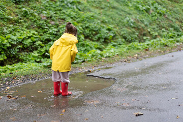 Playful girl wearing yellow raincoat while jumping in puddle during rainfall