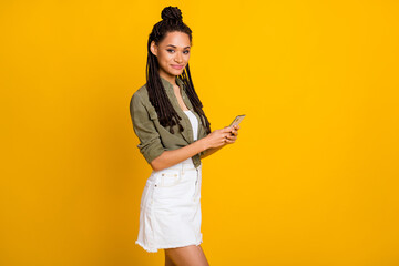 Photo portrait of serious woman holding phone in two hands isolated on vivid yellow colored background