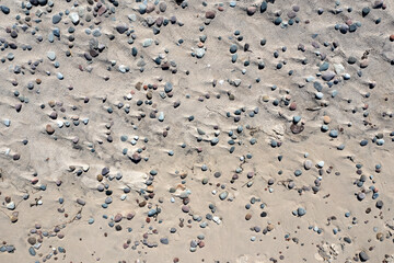 Texture of stones lying on a sandy beach on a sunny day.