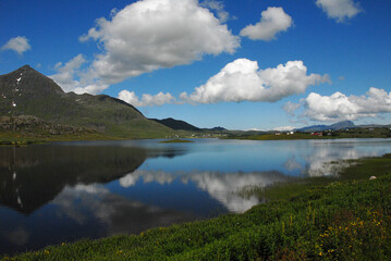 Naklejka na ściany i meble Sea and mountains in Lofoten, Norway. The sky is clear blue with white cotton clouds.