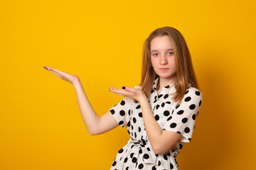 Smiling girl gives advice and points right, promots product, on yellow background, indicates at...