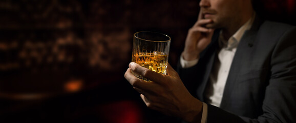 man wearing suit sits in the luxury bar in gentlemen club and drink whiskey. copy space - obrazy, fototapety, plakaty