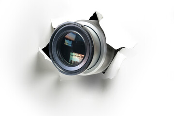 Concept of paparazzi or hidden camera, camera lens looks out through a hole in white paper wall