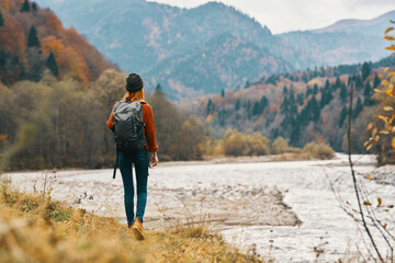 woman on the river bank in the mountains in the autumn forest in nature back view