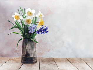 Spring bouquet of yellow narcissus and blue and purple hyacinth in glass vase on rustic wooden background