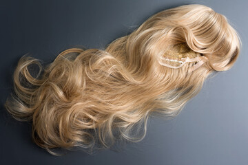 Naklejka premium Female blonde wig close up on grey background. Golden human hair weaves, extensions and wigs. Woman beauty concept.