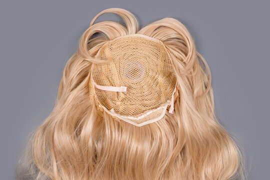 Female blonde wig close up on grey background. Golden human hair weaves, extensions and wigs. Woman beauty concept.