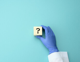 wooden cube with a question mark in the doctor's hand on a blue background. The concept of finding...