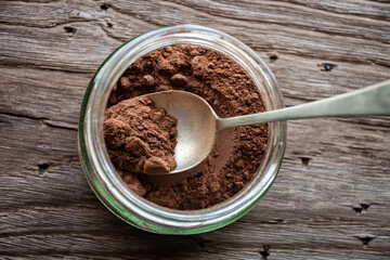cocoa powder in a silver spoon inside of a glass jar