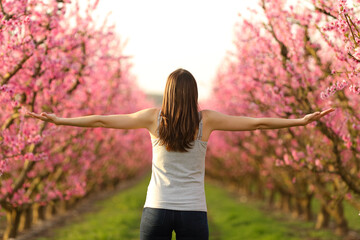Lady stretching arms celebrating spring in a pink field