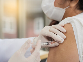 Close-up of a female doctor wearing gloves and using a syringe with cotton to vaccinate a middle-aged female patient, covid-19 or coronavirus vaccine.