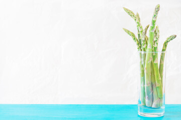 A bunch of asparagus in a transparent glass on a light background