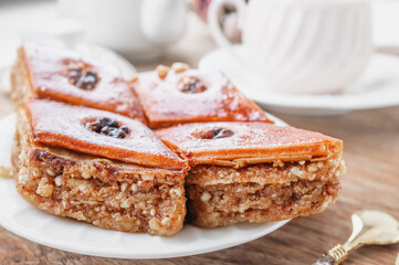 Close-up of baklava. Turkish Ramadan Arabic sweet dessert on a decorative plate, with a coffee cup in the background. Middle Eastern food baklava with nuts and honey syrup