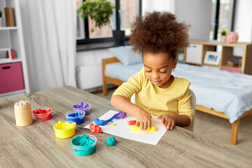 childhood, creativity and hobby concept - little african american girl with modeling clay playing at home