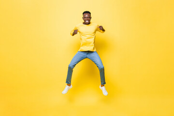 Fototapeta na wymiar Young energetic excited African man jumping and clenching hands on isolated yellow studio background