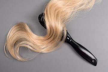 Hairdresser professional hairbrush with curl of blonde hair on grey background. Healthy long blond...