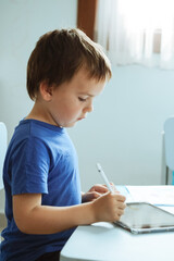 Fototapeta premium Cute boy in blue t shirt using digital tablet or computer for drawing his picture, using stylus . New technology art, online education
