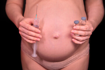 A pregnant woman on a black background with a vaccination syringe in her hand. Pregnancy problem concept