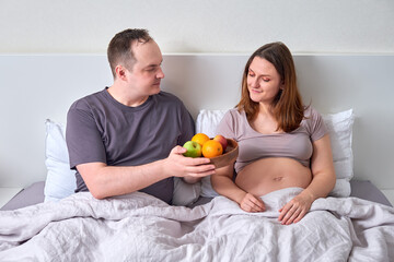 Obraz na płótnie Canvas A man gives a pregnant woman a tray with a plate of fruit - the concept of proper nutrition during pregnancy, weight control
