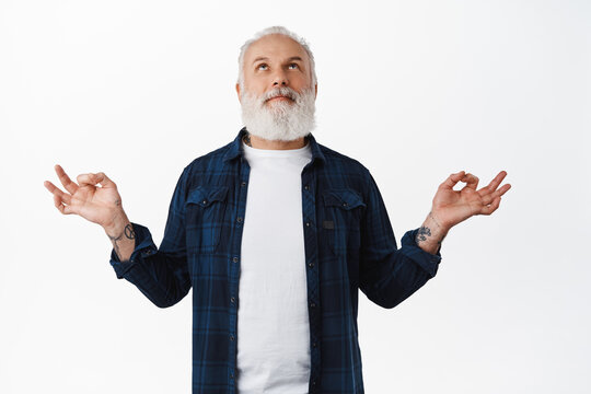 Handsome Old Man With Tattoos Meditating, Smiling While Looking Up And Making Zen Mudra Gesture, Practice Yoga, Breathing Peaceful, Relaxing Mind, Standing Over White Background