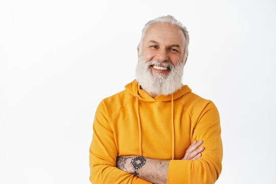 Handsome Old Man With Tattoos Laughing And Smiling Candid, Showing Authentic Emotions, Cross Arms On Chest, Standing Relaxed Against White Background