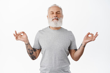Meditation. Smiling mature man meditating, close eyes and breath calm, relaxing with yoga, spread hands sideways in zen om gesture, feeling peace inside, standing over white background - Powered by Adobe