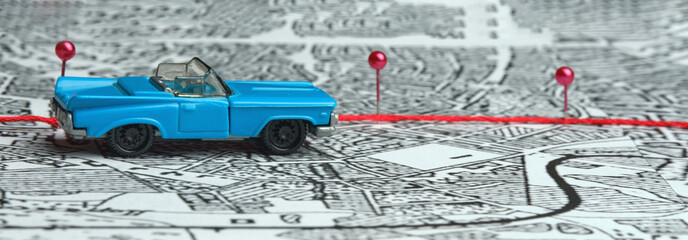 Concept. Following the route. A toy blue convertible is driving across the map. The direction is indicated by red safety pins. Finding a path, a goal, a road.