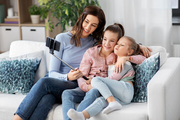 Fototapeta premium family, technology and people concept - happy mother and two daughters with smartphone taking selfie at home