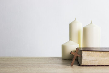 Three candle light with Bible and a wooden cross on a table.