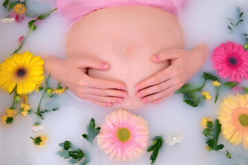 Obraz na płótnie Canvas Pregnant woman holding her belly with hands in a bath with flowers