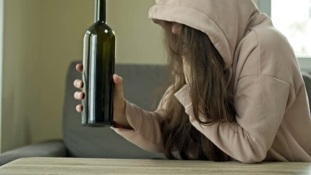 An unkempt woman is drinking wine from a bottle alone. The social problem of female alcoholism.