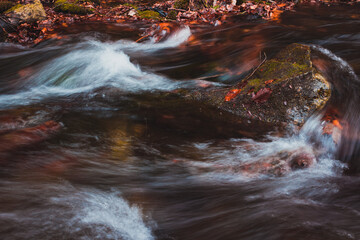 Long exposure photo of the mountain creek with rocks and leaves