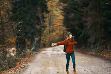 happy woman hiker with backpack walks on the road in autumn forest