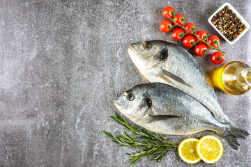 Fresh fish dorado on grey concrete background with ingredients for cooking