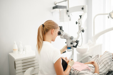 A dentist is looking in a special microscope for dentist in a laboratory wit patient sit in the...