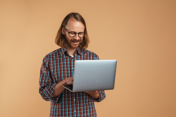 Smiling ginger man wearing eyeglasses holding and using laptop