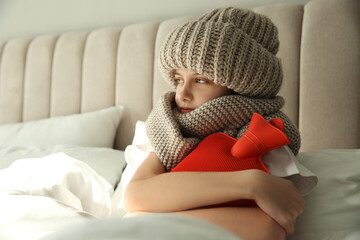 Ill girl with hot water bottle suffering from cold in bed at home