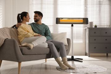Young couple sitting on sofa near electric heater at home