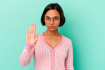 Young mixed race woman isolated on blue background standing with outstretched hand showing stop sign, preventing you.