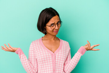 Young mixed race woman isolated on blue background doubting and shrugging shoulders in questioning...