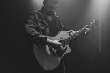 Guitarist playing acoustic guitar in a dark smoky room.