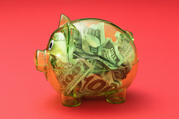 Transparent piggy bank full of dollars on red background