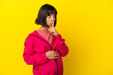 Young pregnant woman over isolated yellow background showing a sign of silence gesture putting finger in mouth