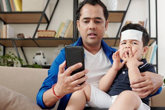 Nervous Indian man with sick naughty son making phone call to pediatrician