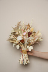 Woman holding beautiful dried flower bouquet on beige background, closeup