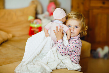 Adorable cute little toddler girl playing with doll. Happy healthy baby child having fun with role game, playing mother at home or nursery. Active daughter with toy.