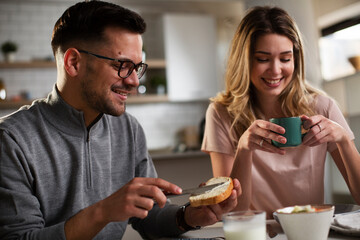 Happy girl enjoying in breakfast with her boyfriend. Loving young couple drinking coffee and eating sandwich at home..
