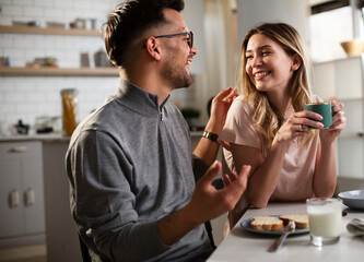Happy girl enjoying in breakfast with her boyfriend. Loving young couple drinking coffee and eating sandwich at home..