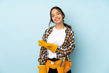 Young electrician woman isolated on blue background presenting an idea while looking smiling towards